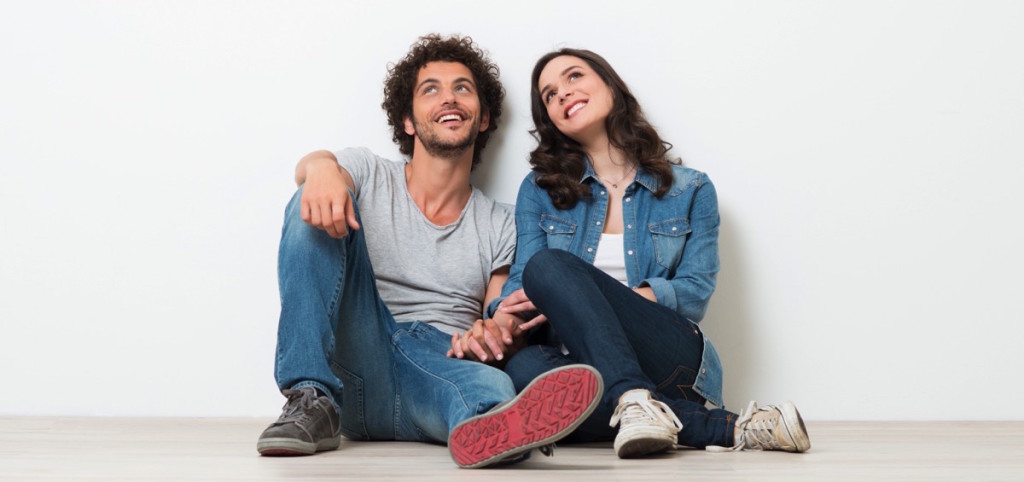 una pareja sentada en el piso agarrada de la mano mirando hacia arriba pensando