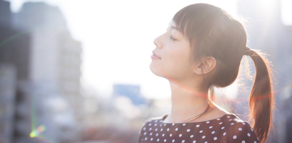 Mujer feliz con los ojos cerrados respirando hondo con fondo desenfocado