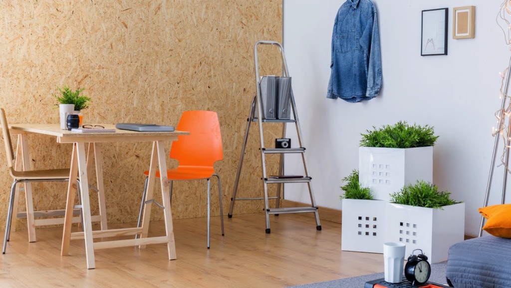 Habitación con piso de madera, comedor de madera, macetas y una escalera decorativa con cámara y libros