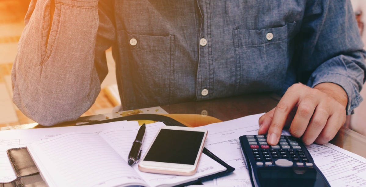 hombre usando una calculadora, su celular y una agenda con pluma