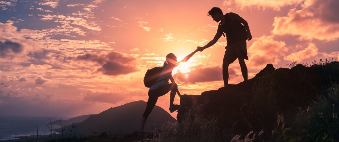 Pareja escalando una montaña con un atardecer de fondo