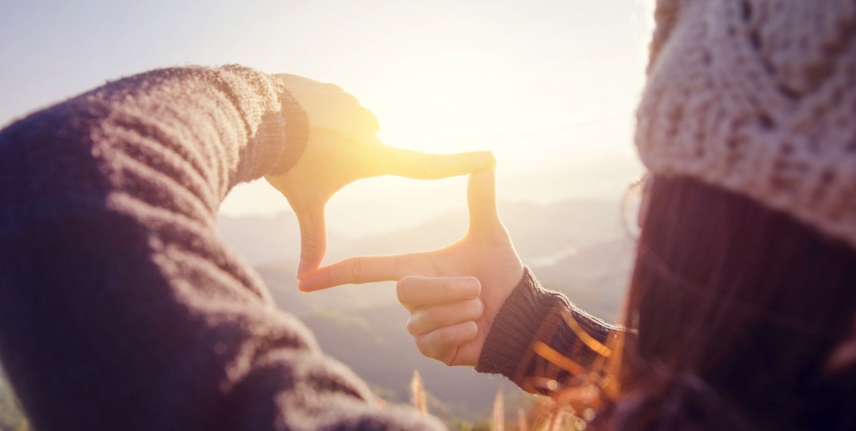 Mujer enfocando el sol con sus manos