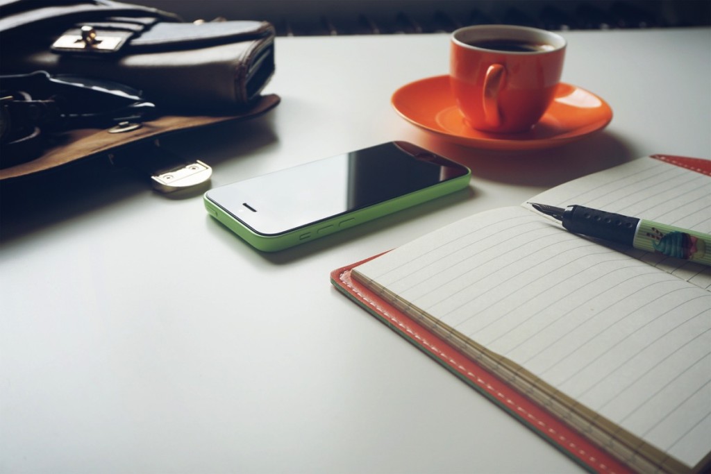 escritorio con café, celular y libreta con pluma